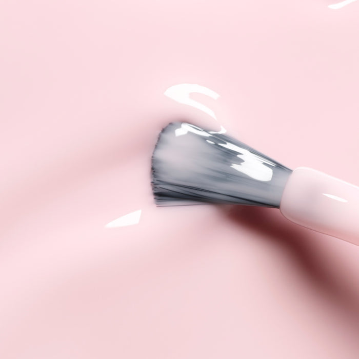 A close-up of a makeup brush with white bristles spreading Manucurist's Milky Pink, a creamy, glossy gel polish, over a smooth, light pink surface.