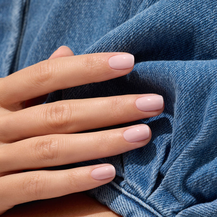 A close-up of neatly manicured nails painted in Manucurist’s Milky Pink, resting on blue denim—showcasing the elegant look of this soft gel polish shade.