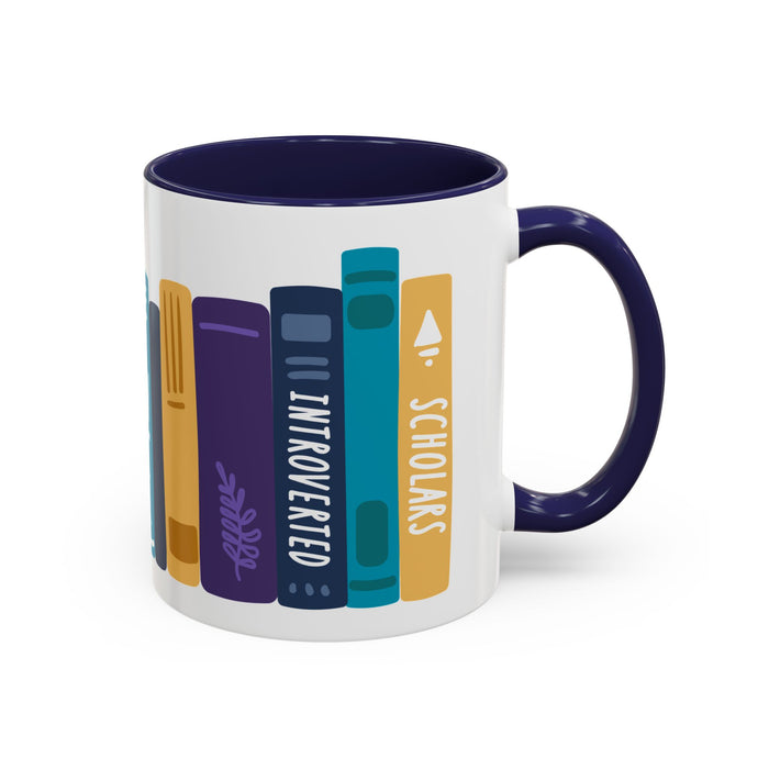 A white ceramic mug with a navy blue handle and interior, featuring a colorful graphic of vertically standing books with titles like "INTROVERTED" and "SCHOLARS" in a playful, minimalist design.