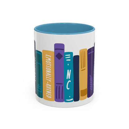 A white ceramic mug with a blue interior featuring a colorful graphic of book spines in shades of purple, teal, and gold, designed by thtgrlreads for book lovers.
