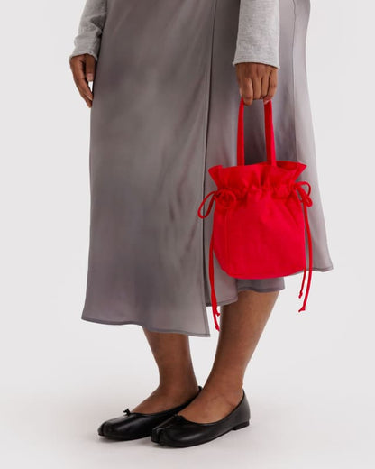 Red nylon drawstring bag with gathered top, held in hand