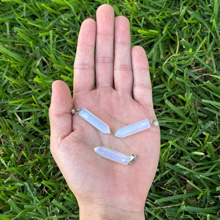 Opalite crystal point pendants displayed in the palm of a hand for size reference.