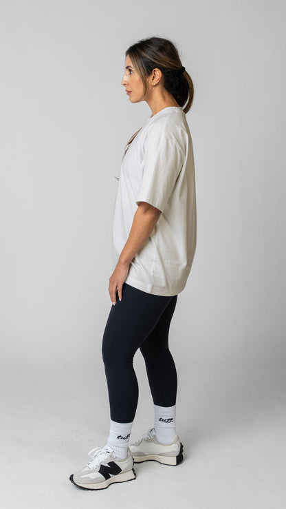 Woman wearing a plain white t-shirt and dark tights on a light gray background. Side view