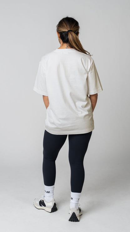 Woman wearing a plain white t-shirt and dark tights on a light gray background. Back view.