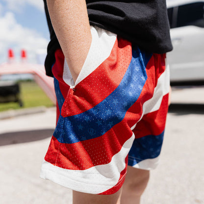 Close-up of youth model in red white and blue Patriot Pitch shorts showing diagonal colorblock and star pattern detail with hand in pocket at outdoor event