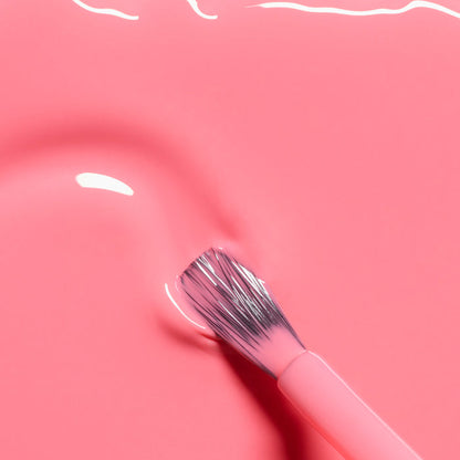 A close-up of a brush with pink bristles resting on the smooth, glossy surface of Manucurist's Pop LED Gel nail polish in a vibrant electric pink shade with a shiny, reflective finish.