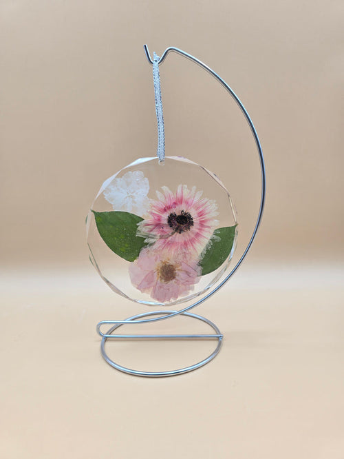 Preserved flowers in a clear resin circle ornament on a silver ribbon and stand