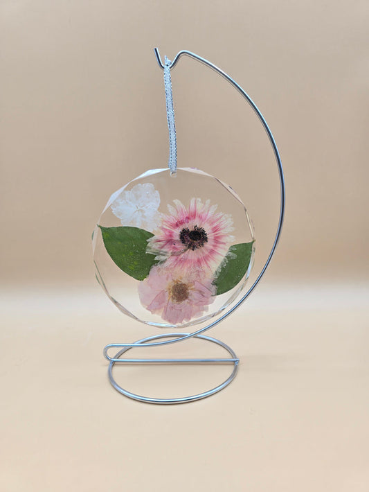 Preserved flowers in a clear resin circle ornament on a silver ribbon and stand