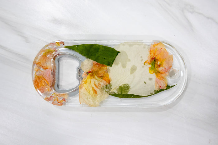 Wide landscape photo of a pressed flower bottle opener displayed on a styled surface