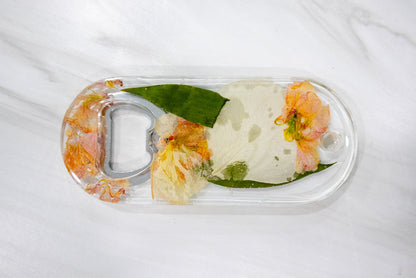 Wide landscape photo of a pressed flower bottle opener displayed on a styled surface