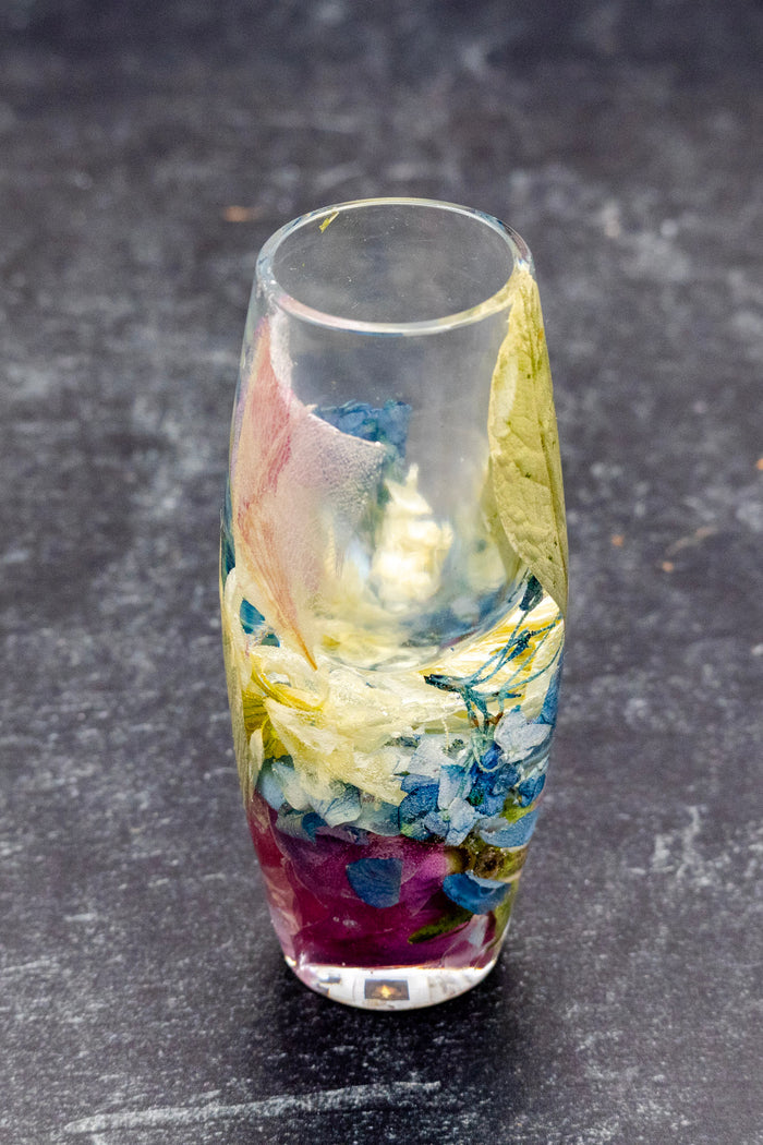 Tall portrait photo of a pressed flower teardrop necklace with mixed dried flowers on a dark background