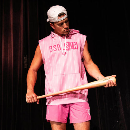 Adult male model holding a wood bat wearing the pink Jackson Olson x BL101 Pro Series Shorts V2 paired with a matching pink pinstripe sleeveless hoodie