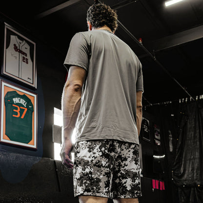 Person wearing a gray t-shirt and camouflage shorts in a locker room setting.