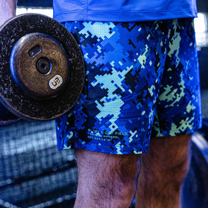 Person wearing blue digital camouflage shorts holding a barbell in a gym setting
