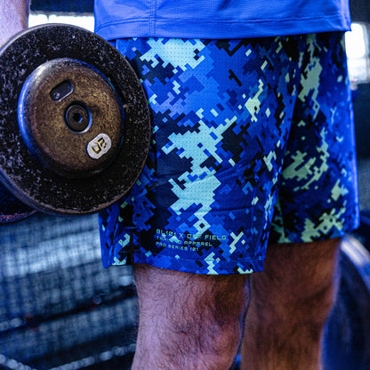 Person wearing blue digital camouflage shorts holding a barbell in a gym setting