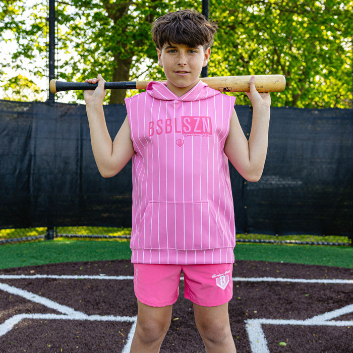 Youth player holding a bat over his shoulders wearing the pink Jackson Olson x BL101 Pro Series Shorts V2 paired with a matching pink pinstripe sleeveless hoodie