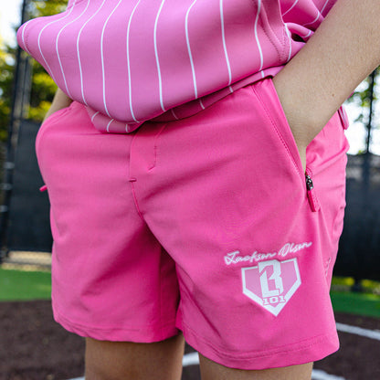 Close-up of the youth pink Pro Series Shorts V2 showing the "Jackson Olson" script, BL101 home plate logo, and zip side pocket