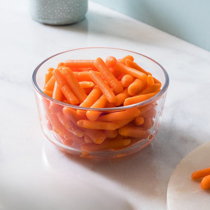 Clear glass bowl filled with orange carrot-like snacks on a light surface.