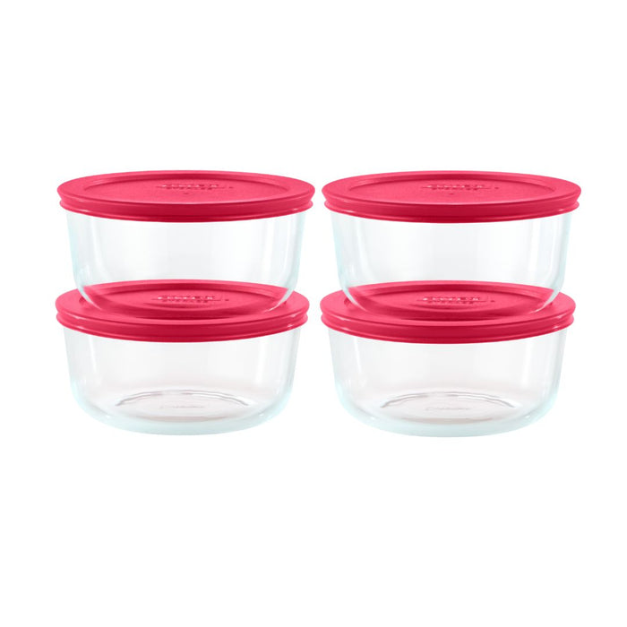 Set of four clear glass food storage containers with pink lids on a white background
