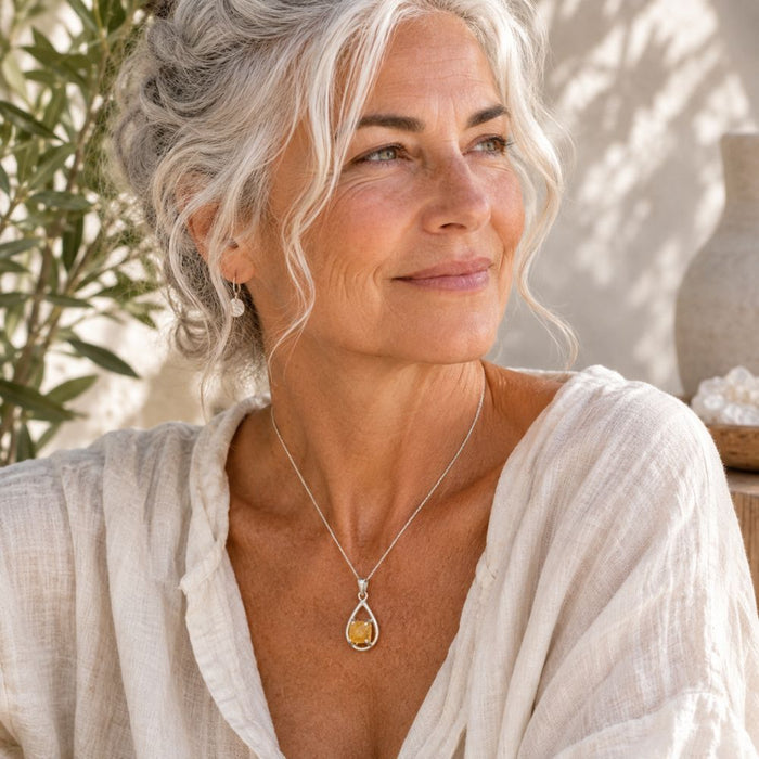Wwoman with white hair wearing a Raw Citrine Silver Teardrop Pendant on a delicate silver chain with a soft cream linen blouse.