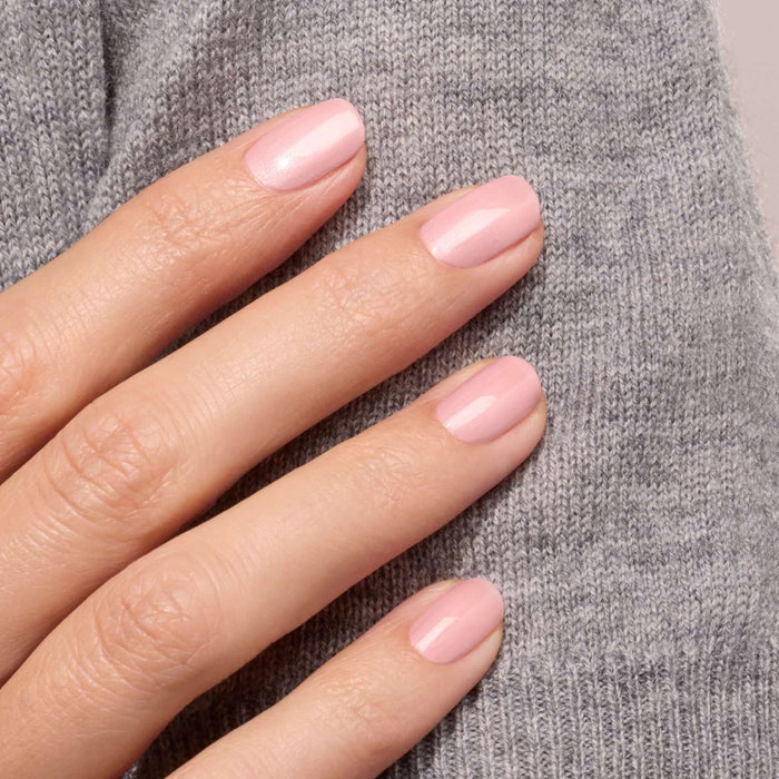 A hand with neatly manicured nails painted in Manucurist's Satin, a glossy pale pink nail polish, rests against soft light gray knit fabric.