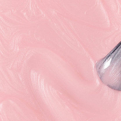 A close-up of Manucurist's Satin, a glossy, creamy pale pink nail polish with a pearly finish, being swirled by a clear spatula on a smooth surface. The polish looks soft and shiny.