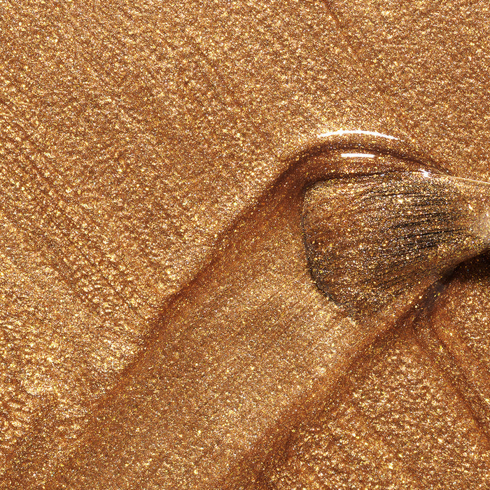 A makeup brush glides through Manucurist Shimmer, creating a textured, sparkling gold finish—perfectly complemented by cool undertone nail polish for a chic, sophisticated look.