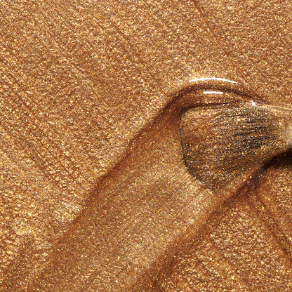 A makeup brush glides through Manucurist Shimmer, creating a textured, sparkling gold finish—perfectly complemented by cool undertone nail polish for a chic, sophisticated look.