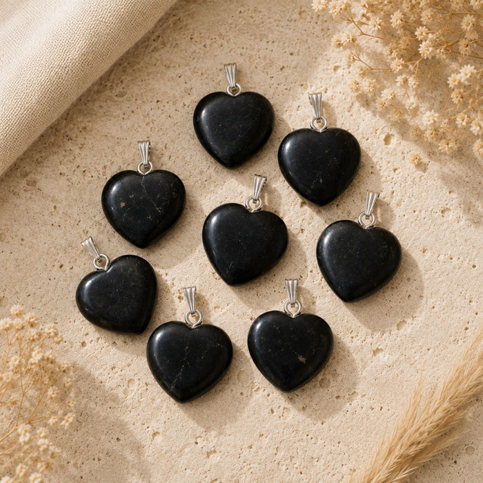 Natural Shungite heart pendants with silver bails displayed on a warm neutral stone surface.