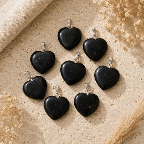 Natural Shungite heart pendants with silver bails displayed on a warm neutral stone surface.