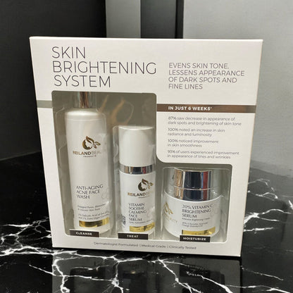 Front view of Reiland Advanced Skin Brightening System featuring cleanser, calming serum, and vitamin C brightening cream in boxed packaging. Positioned on a black marble surface with clear product claims highlighting improvements in skin tone, luminosity, and fine lines within 6 weeks.