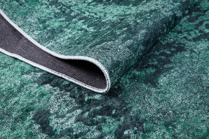 A close-up of the Smokey Mountains - Washable Rug - JR1631 in green and black, featuring textured weave, a flipped corner revealing the dark underside, and a stitched white edge—ideal for high-traffic spaces.