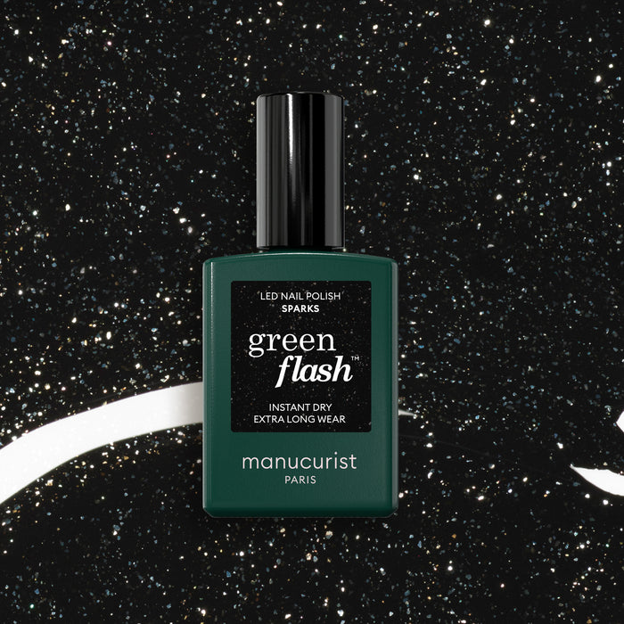 A bottle of Manucurist Sparks gel polish stands upright against a black backdrop dotted with white speckles resembling stars.