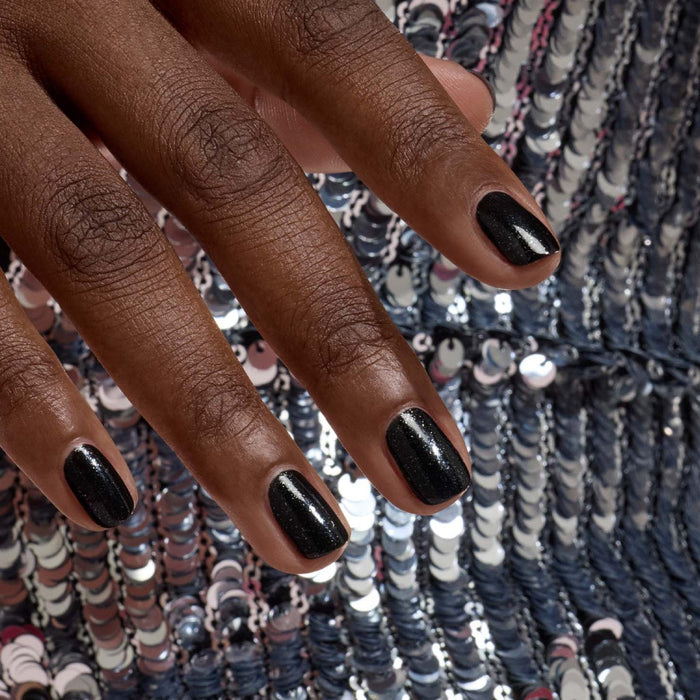 A hand with short, neatly manicured nails painted in Manucurist’s Sparks rests on shiny silver sequins, creating a striking, shimmering look.