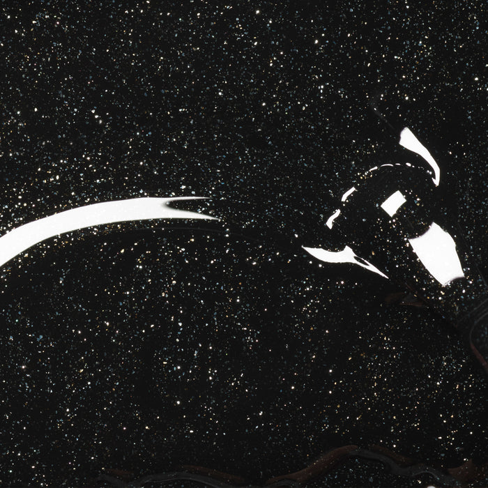 A lightbulb rests on Manucurist's Sparks, a shiny black glitter gel polish surface resembling a starry night sky, with reflections highlighting the bulb and sparkling particles scattered throughout.