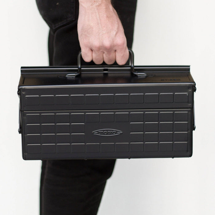 Black steel cantilever toolbox with top handle, held by hand.