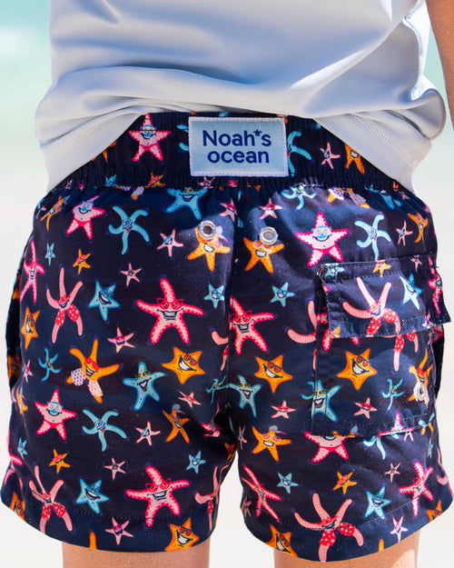 Super Starfish Kinder-Badehose von Noah*s Ocean, Rueckansicht mit Logo-Label am Strand