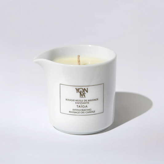 Taiga Massage Oil Candle 125g glass jar with wooden lid beside pine sprigs highlighting sesame shea and mango butter