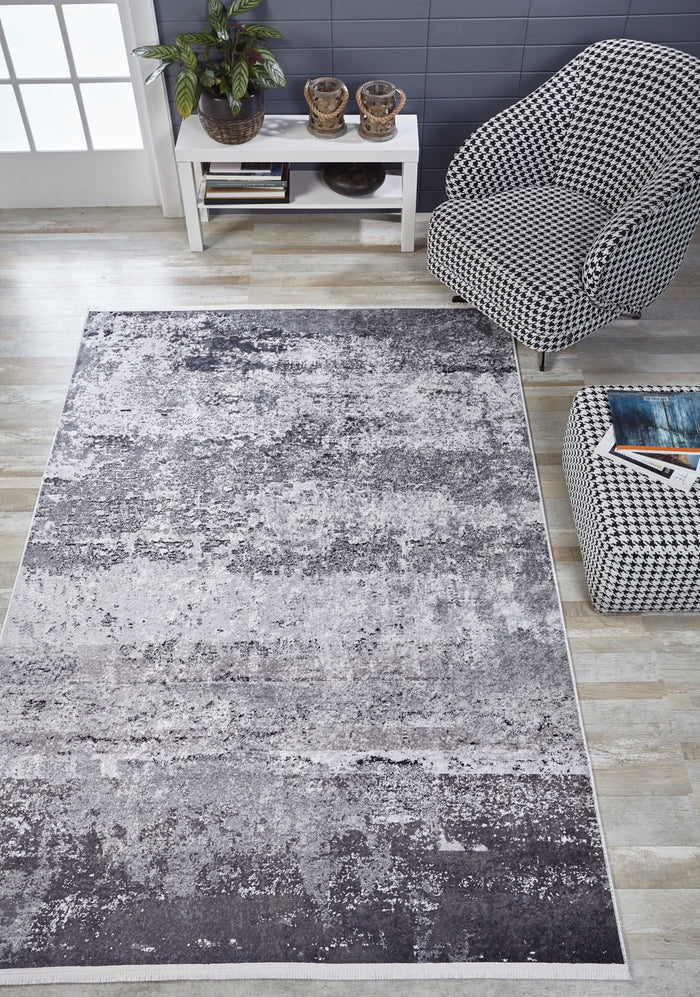 A modern living room with a large Techno Flux - Washable Rug - JR1814 in gray-anthracite, a houndstooth-patterned chair and ottoman, white console table with plants and decor, and light wood flooring.