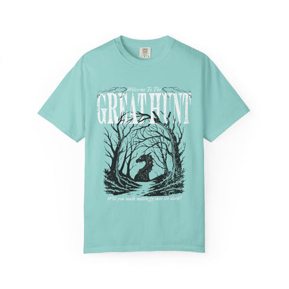 A vintage wash Comfort Colors graphic tee from thtgrlreads featuring a dark fantasy design of a silhouetted figure within twisted trees and text reading "Welcome to The Great Hunt," part of the Tees and Hollow collections.