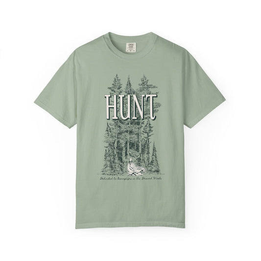 Thtgrlreads The Poison Daughter collection features a sage green Comfort Colors graphic tee with vintage wash and a detailed forest scene surrounding the large "HUNT" text in a classic font.