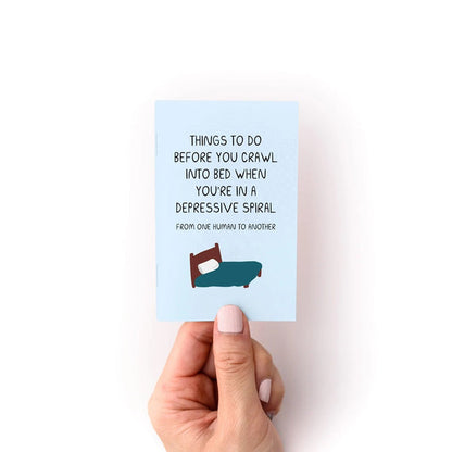 Zine booklet with teal front cover text about crawling into bed; illustrated bed icon