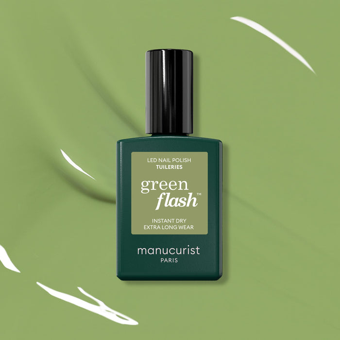 A bottle of Manucurist Tuileries Green Flash Gel Polish is showcased on a green background with white paint streaks, its label highlighting Instant Dry and Extra Long Wear—echoing the elegance of Paris gardens.