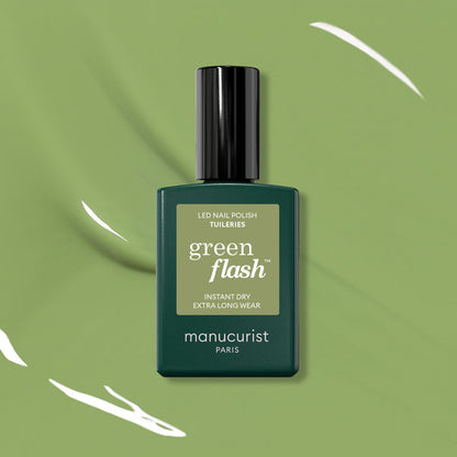 A bottle of Manucurist Tuileries Green Flash Gel Polish is showcased on a green background with white paint streaks, its label highlighting Instant Dry and Extra Long Wear—echoing the elegance of Paris gardens.