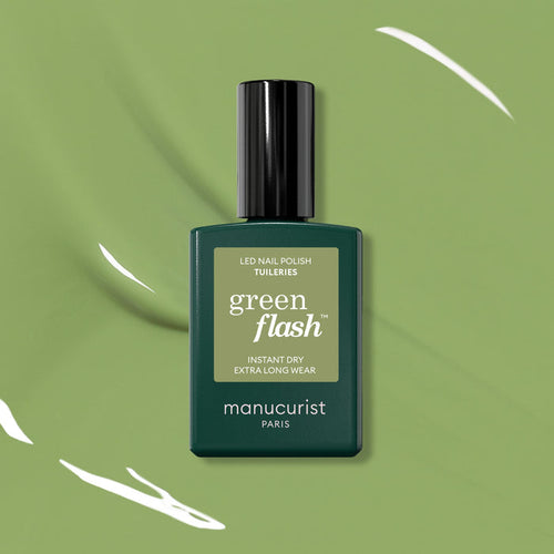 A bottle of Manucurist Tuileries Green Flash Gel Polish is showcased on a green background with white paint streaks, its label highlighting Instant Dry and Extra Long Wear—echoing the elegance of Paris gardens.
