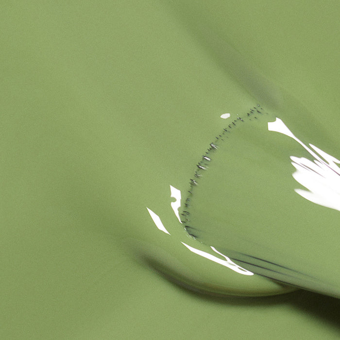 A close-up of Manucurist's Tuileries shows its smooth, glossy light olive green surface, featuring a curved section and reflected white highlights.