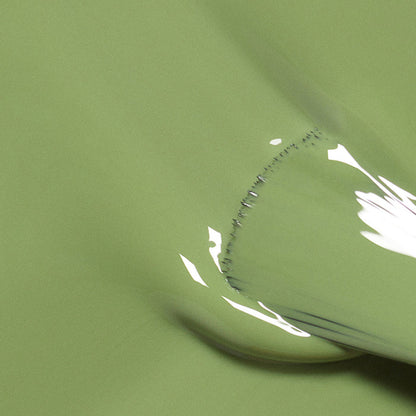 A close-up of Manucurist's Tuileries shows its smooth, glossy light olive green surface, featuring a curved section and reflected white highlights.
