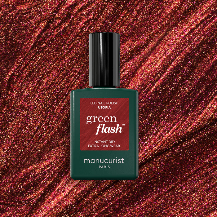 A bottle of Manucurist Utopia gel polish stands against a sparkling, deep red glittery background. The bottle is dark green with a black cap and red label.